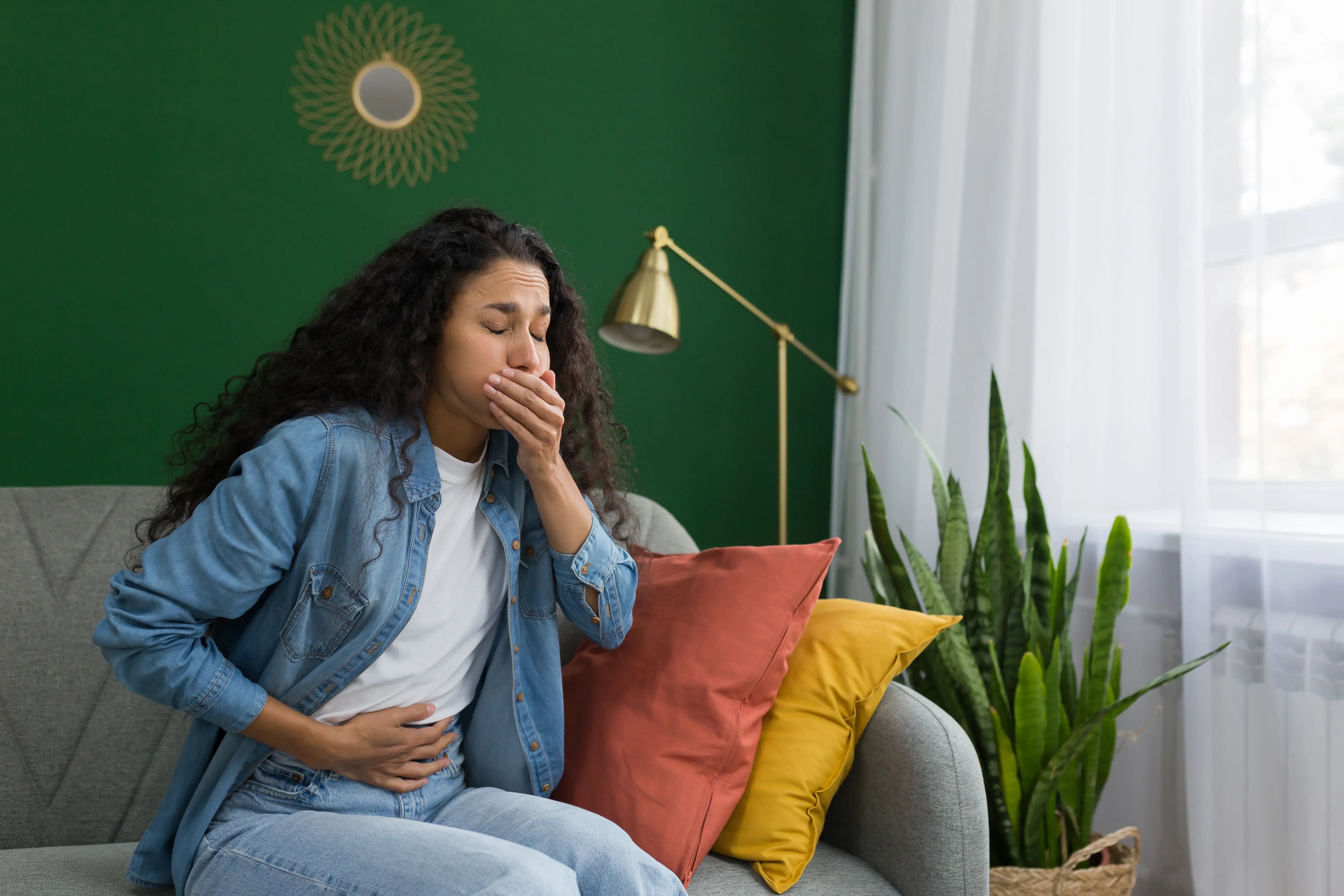 Young beautiful lady with nausea sat on sofa at home 